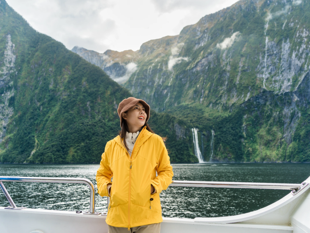 Woman in a yellow rain jacket standing on the deck of a sightseeing boat in Milford Sound.