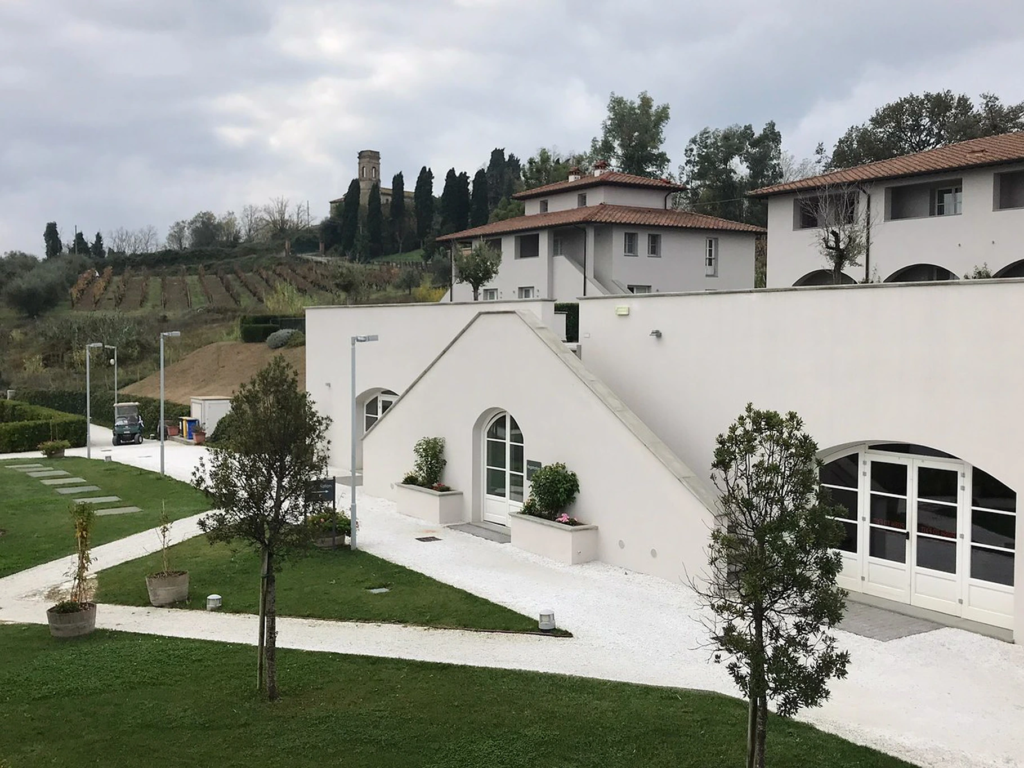 Beautiful white stucco villa architecture and rolling vineyards at Borgo alle Vigne under an overcast sky.