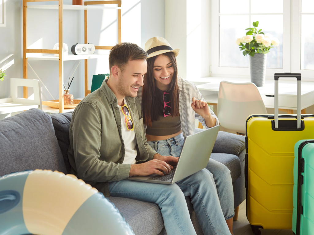 Couple sitting on a gray couch using a laptop, surrounded by bright yellow and green luggage.