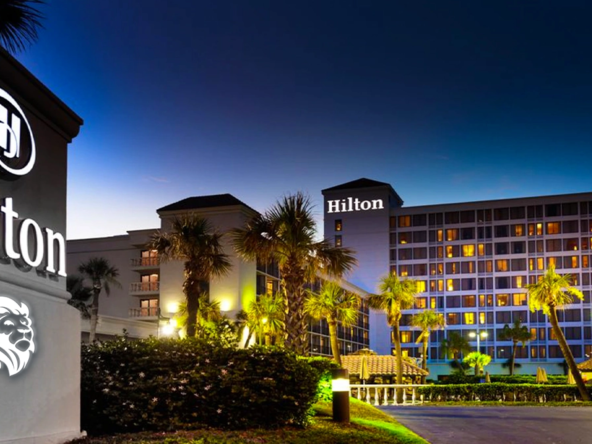 Illuminated exterior facade and palm trees at Galveston Island Resort during a clear evening dusk.