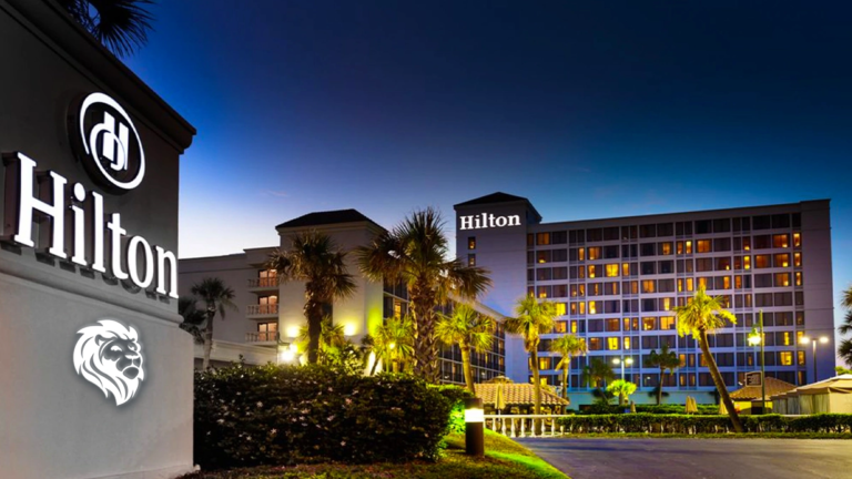 Illuminated exterior facade and palm trees at Galveston Island Resort during a clear evening dusk.