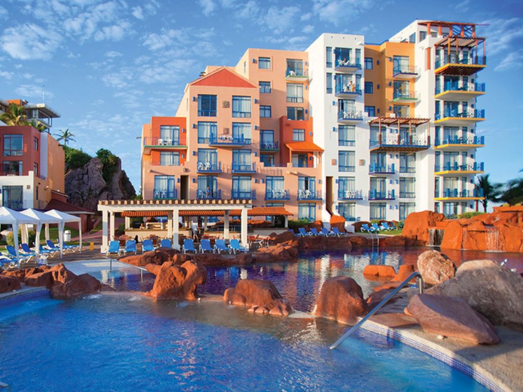 Large pool with rock waterfalls outside the colorful Wyndham El Cid Marina resort building.