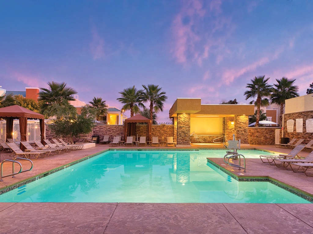 Resort pool surrounded by palm trees, lounge chairs, and cabanas under a pink sunset at Club Wyndham Tropicana Las Vegas.
