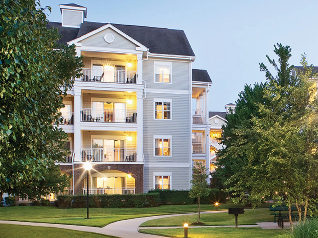Illuminated balconies on a resort building at dusk, featuring a walking path and green lawns at Club Wyndham Nashville.