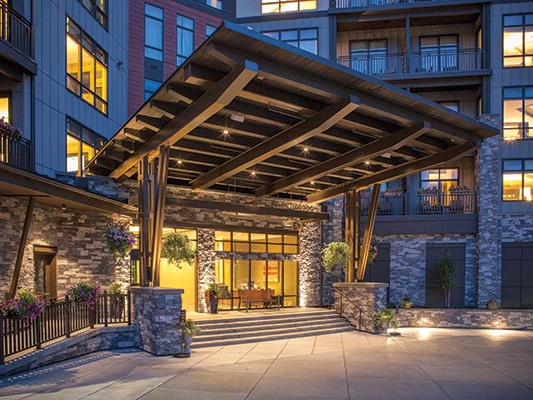 A cozy outdoor patio with tables and chairs, surrounded by greenery and well-lit at dusk.