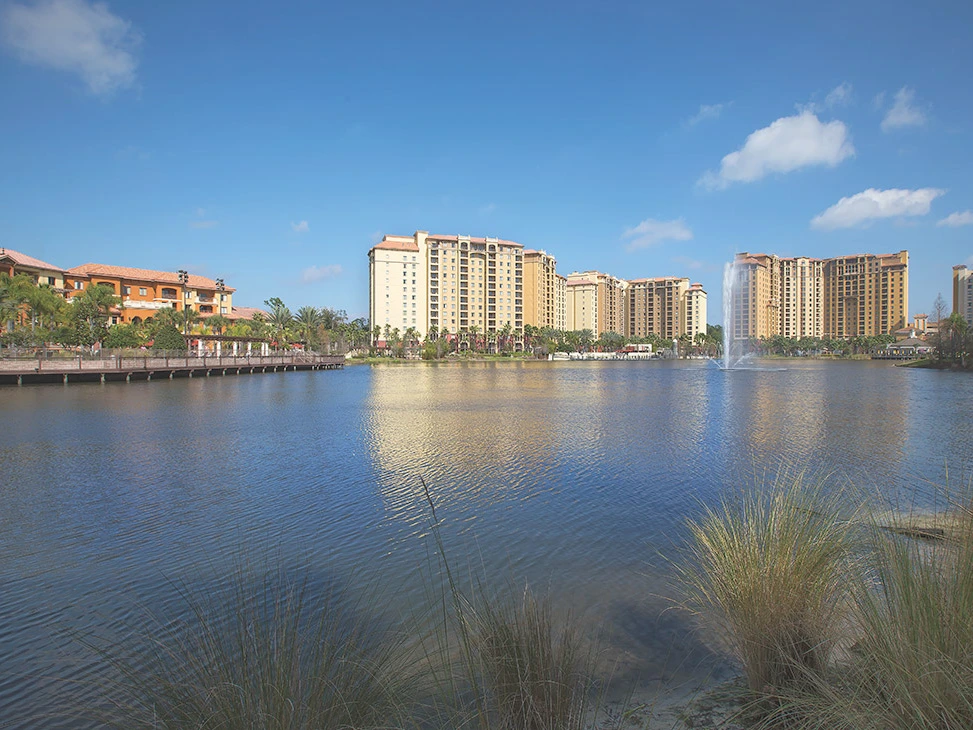 A calm lake reflecting tall buildings and palm trees under a blue sky, illustrating the opportunity to Sell Wyndham Points.