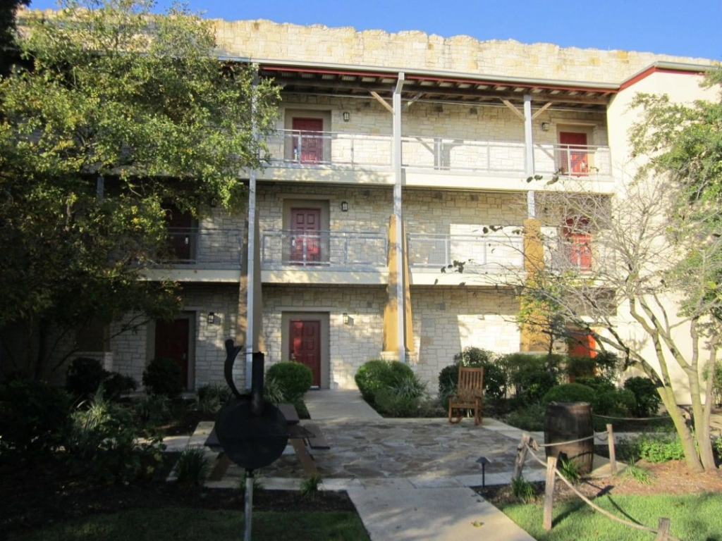 A three-story stone building at Hyatt Wild Oak Ranch with red doors, surrounded by landscaping and a pathway.