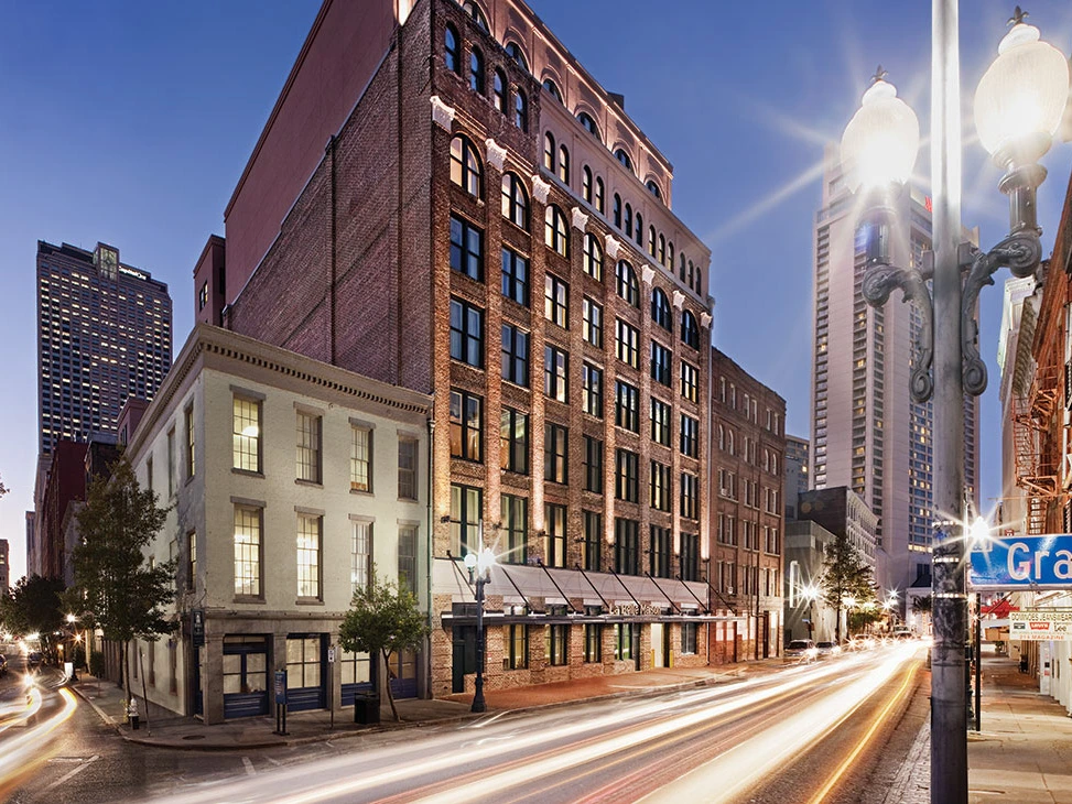 Historic brick building with large windows, streetlights, and blurred cars at dusk.