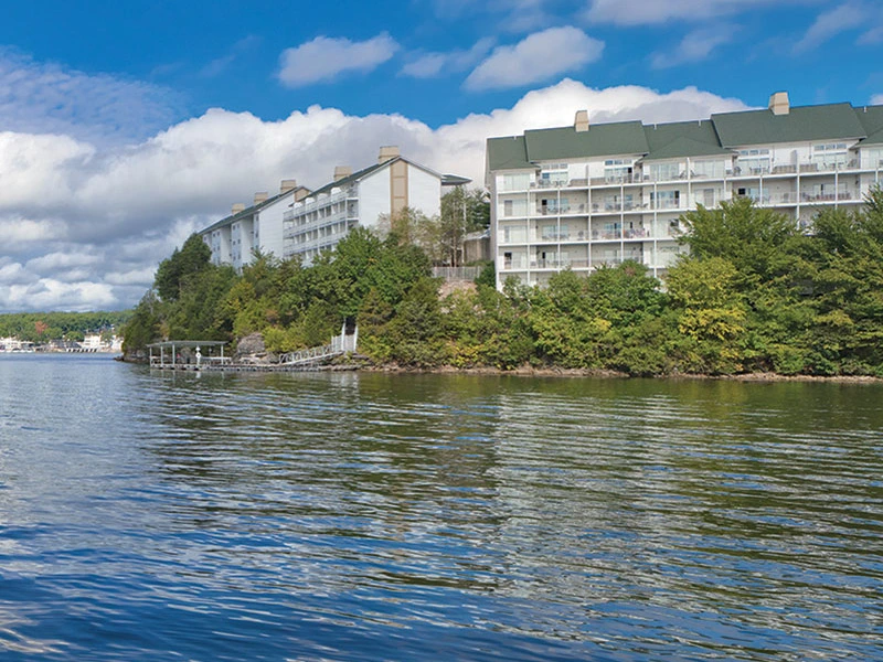 Sell Wyndham Points: a quiet lake with calm water reflecting a cloudy sky, lined by green trees and modern buildings.