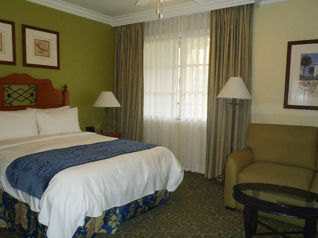 A room at Marriott's Newport Coast Villas with a queen bed, beige walls, a green accent wall, a chair, and window curtains.
