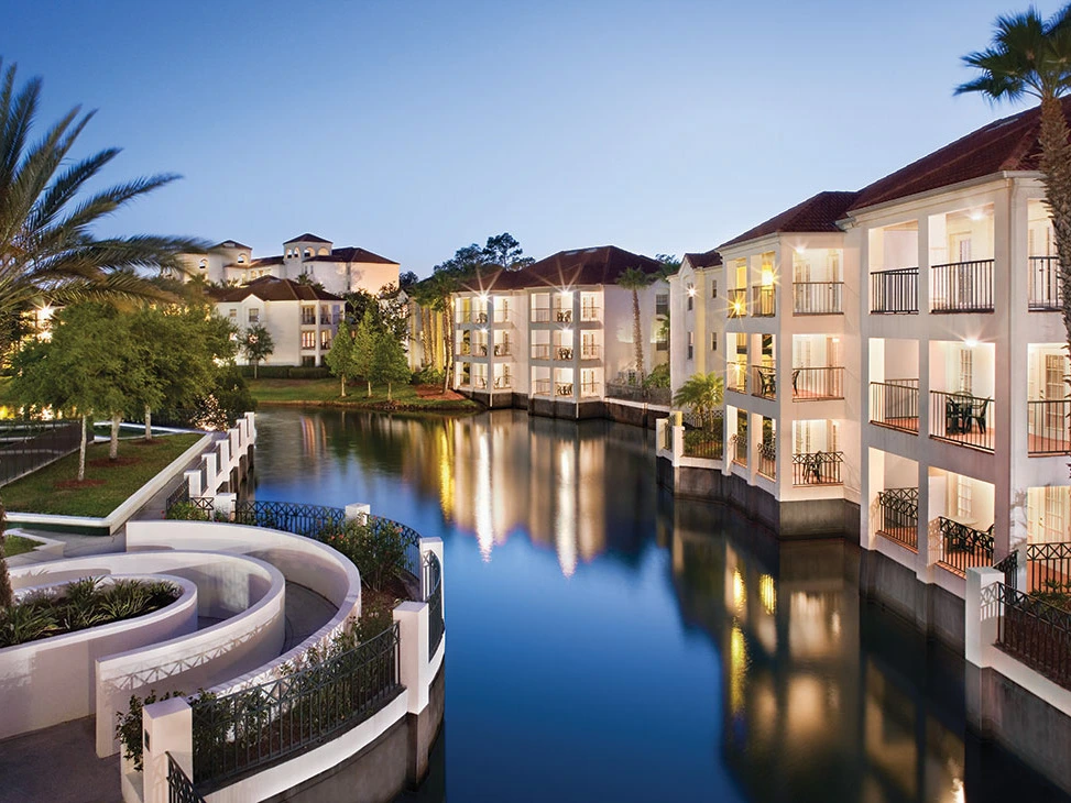 Beautiful view of a calm waterway surrounded by elegant buildings and palm trees at dusk.