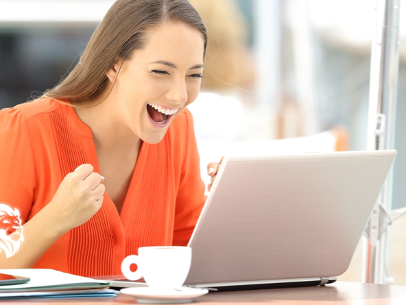 An excited woman in an orange shirt cheering and celebrating in front of her laptop, illustrating a successful user experience with the best place to sell timeshare online.