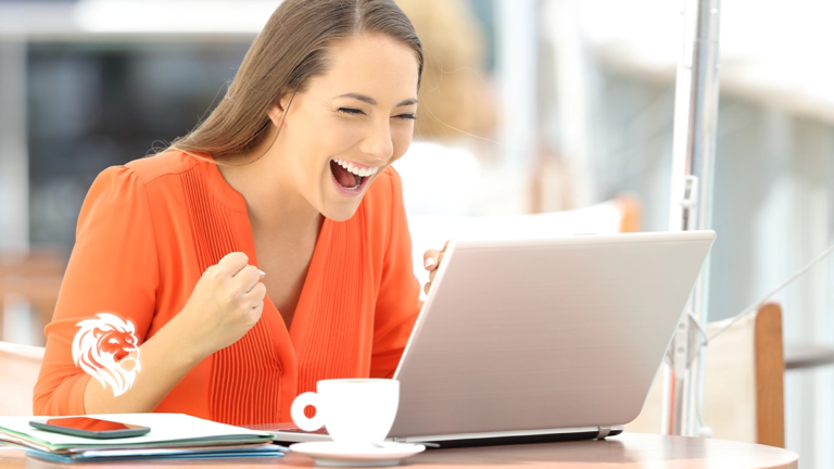 An excited woman in an orange shirt cheering and celebrating in front of her laptop, illustrating a successful user experience with the best place to sell timeshare online.