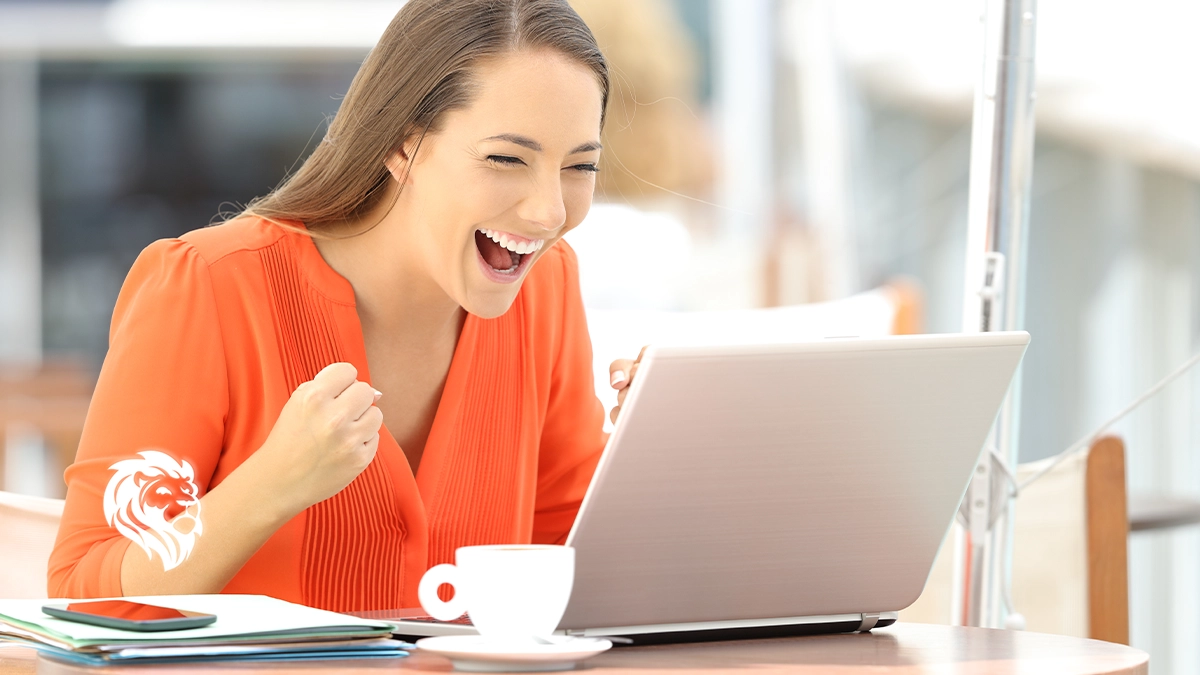 An excited woman in an orange shirt cheering and celebrating in front of her laptop, illustrating a successful user experience with the best place to sell timeshare online.