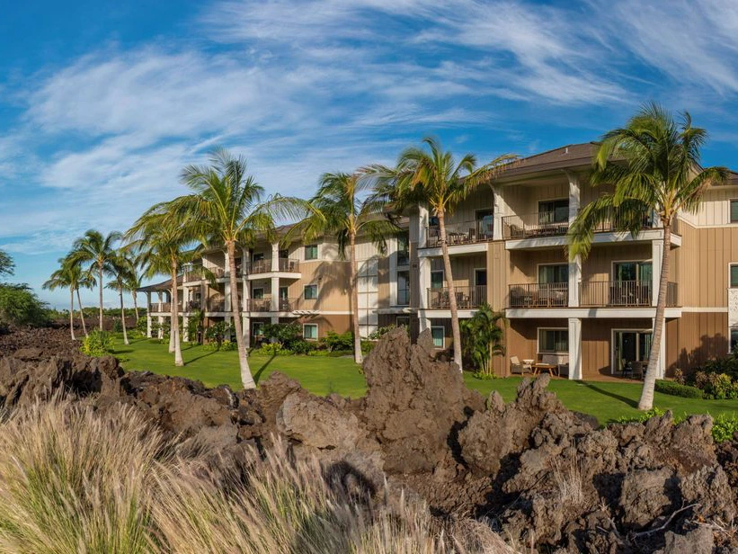 Exterior of Kings' Land by Hilton Grand Vacations resort with palm trees, lawns, and volcanic rock in the foreground.