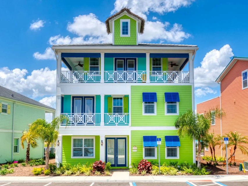 A colorful three-story beach house with green and blue siding and a small roof turret.