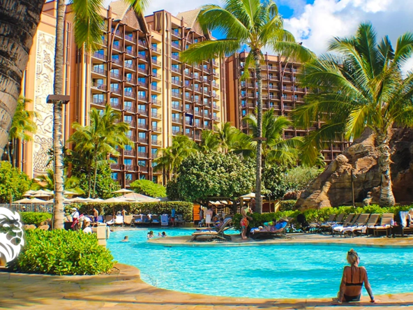 Sunny outdoor swimming pool surrounded by tropical palm trees and tall resort towers at Aulani in Hawaii.