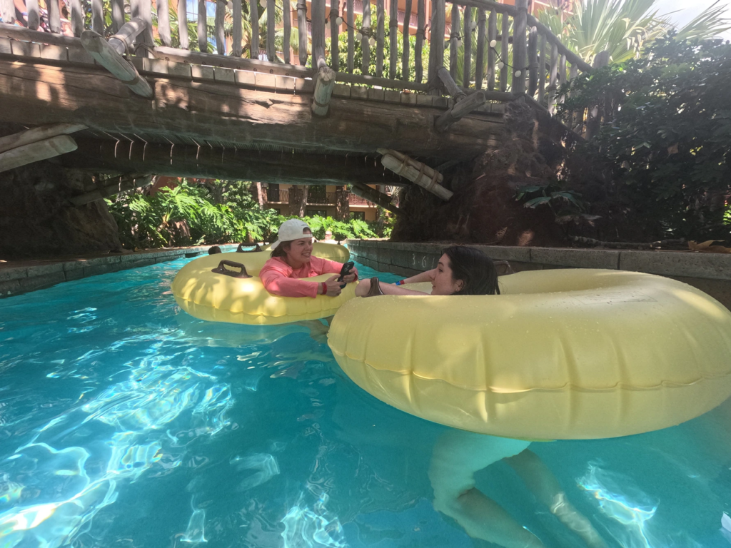Sunny day view of guests riding yellow inner tubes down a winding tropical lazy river at Aulani Disney Vacation Club Villas.