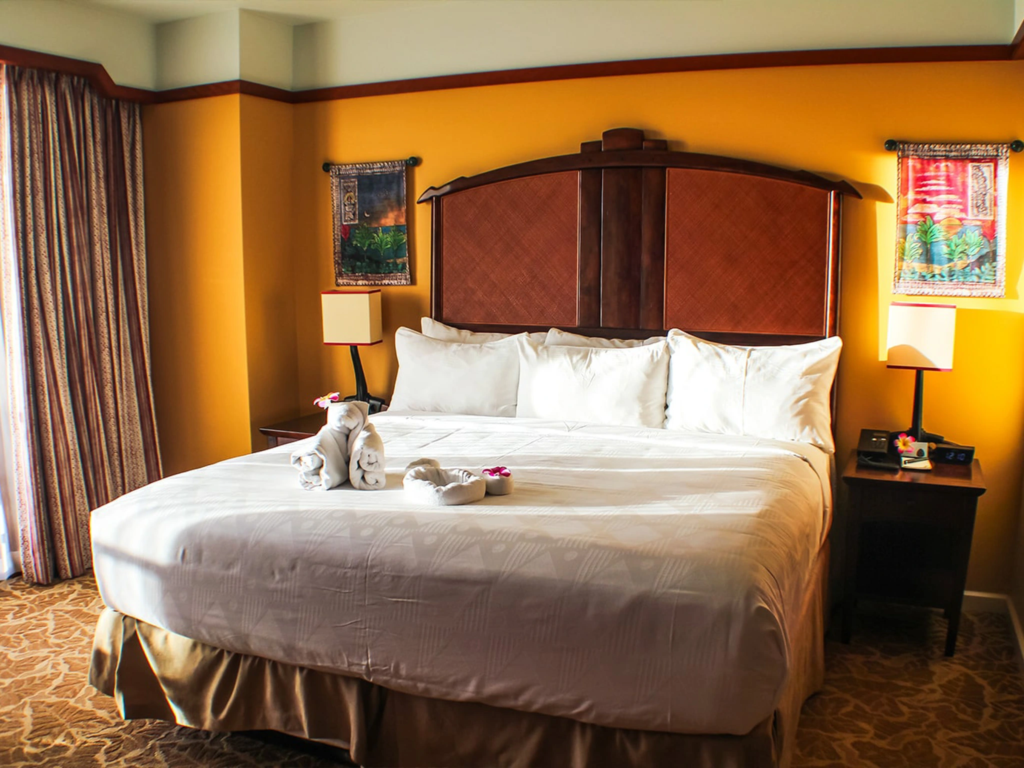 Spacious resort bedroom with a king bed, warm yellow walls, and decorative towel animals on the bed at Aulani Disney Vacation Club Villas
