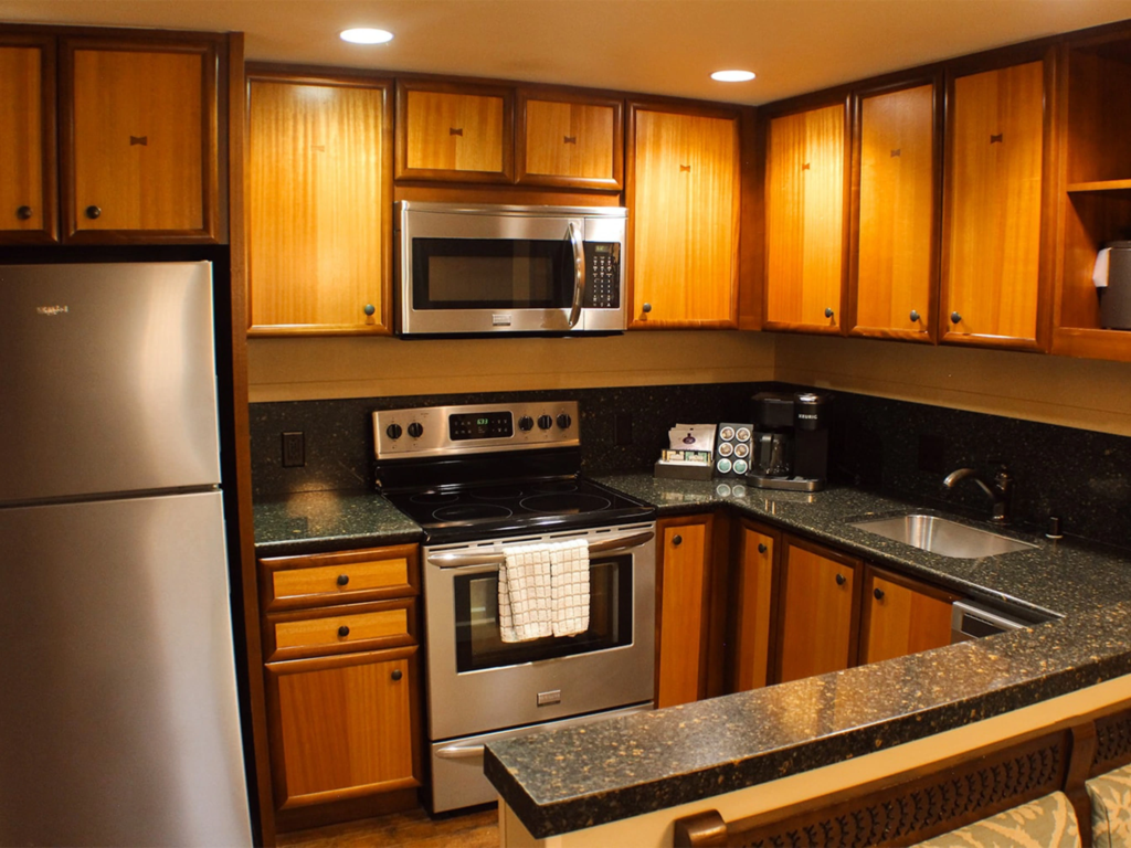A full kitchen inside a resort villa with wood cabinetry, dark countertops, and stainless steel appliances at Aulani.
