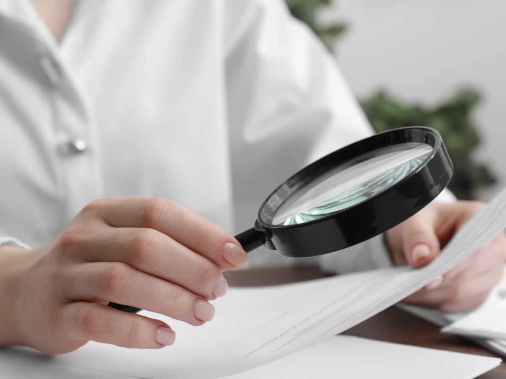 Close-up of a person using a black magnifying glass to carefully inspect a physical document.