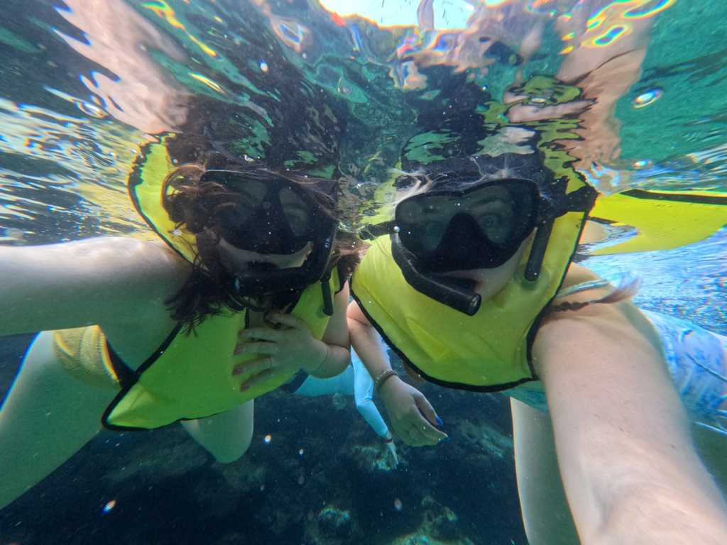 Underwater selfie of two people snorkeling with masks and yellow safety vests at Aulani's Rainbow Reef.