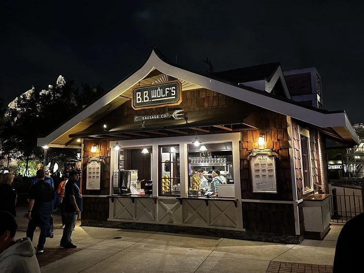 Guests order food at night from the glowing wooden walk-up service counter of B.B. Wolf's kiosk at Disney Springs.