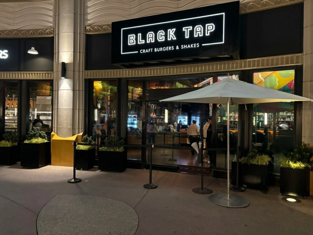 Exterior entrance of Black Tap Craft Burgers & Shakes at night, showing guests entering beneath the marquee.