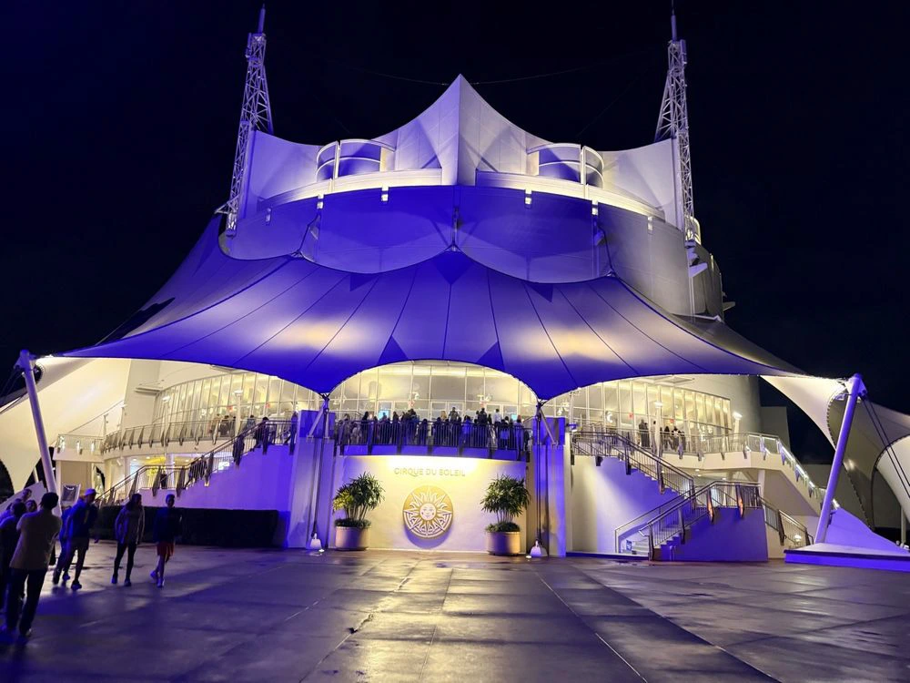 The white permanent tent structure of the Cirque du Soleil theater glows with purple night lighting at Disney Springs.