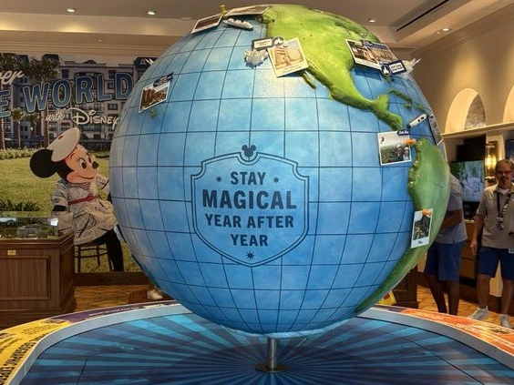 A large decorative globe covered in pinned travel photographs stands inside a bright room near a Minnie Mouse figure.