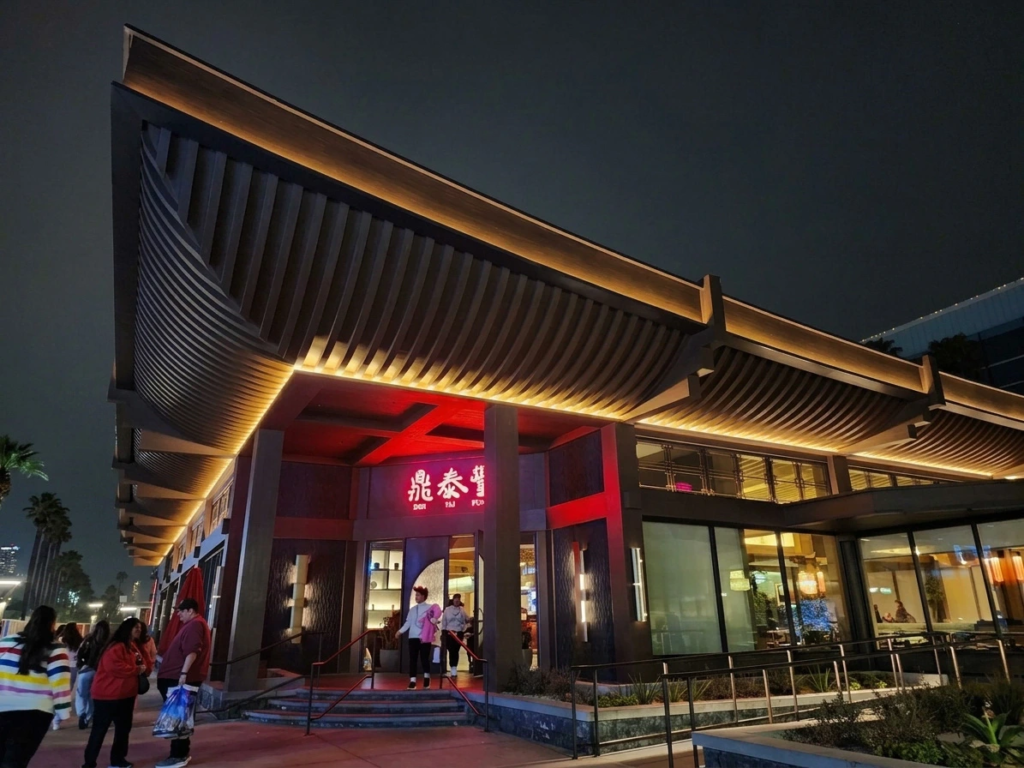 Modern architectural exterior of Din Tai Fung at night, illuminated by warm lighting beneath its distinctive curved roof.