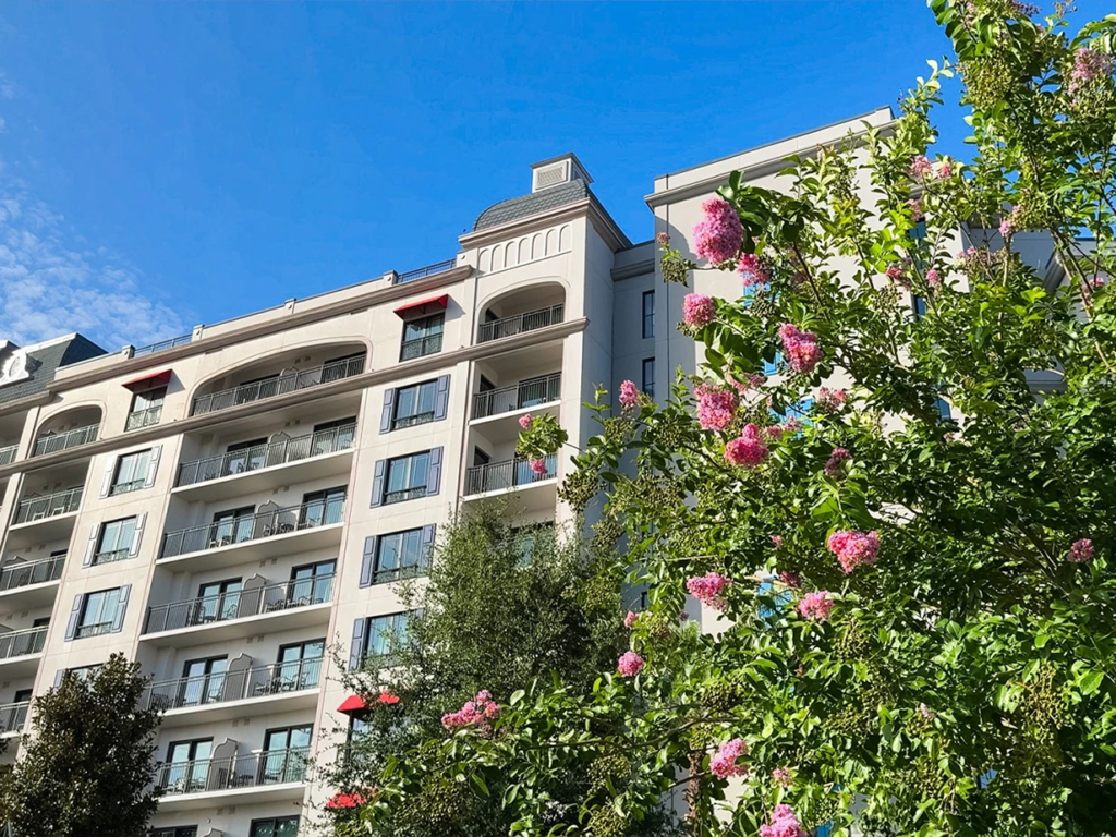 White multi-story exterior facade of Disney's Riviera Resort framed by vibrant pink flowers.