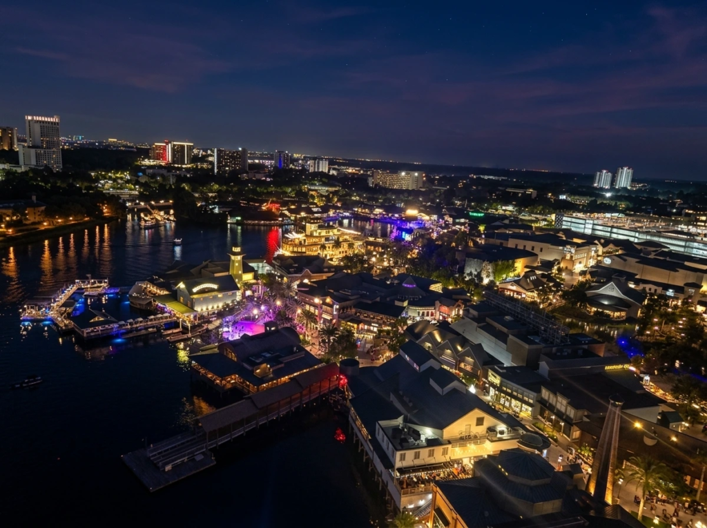Aerial night view of illuminated waterfront venues, pedestrian walkways, and boat docks reflecting in the dark lake waters.