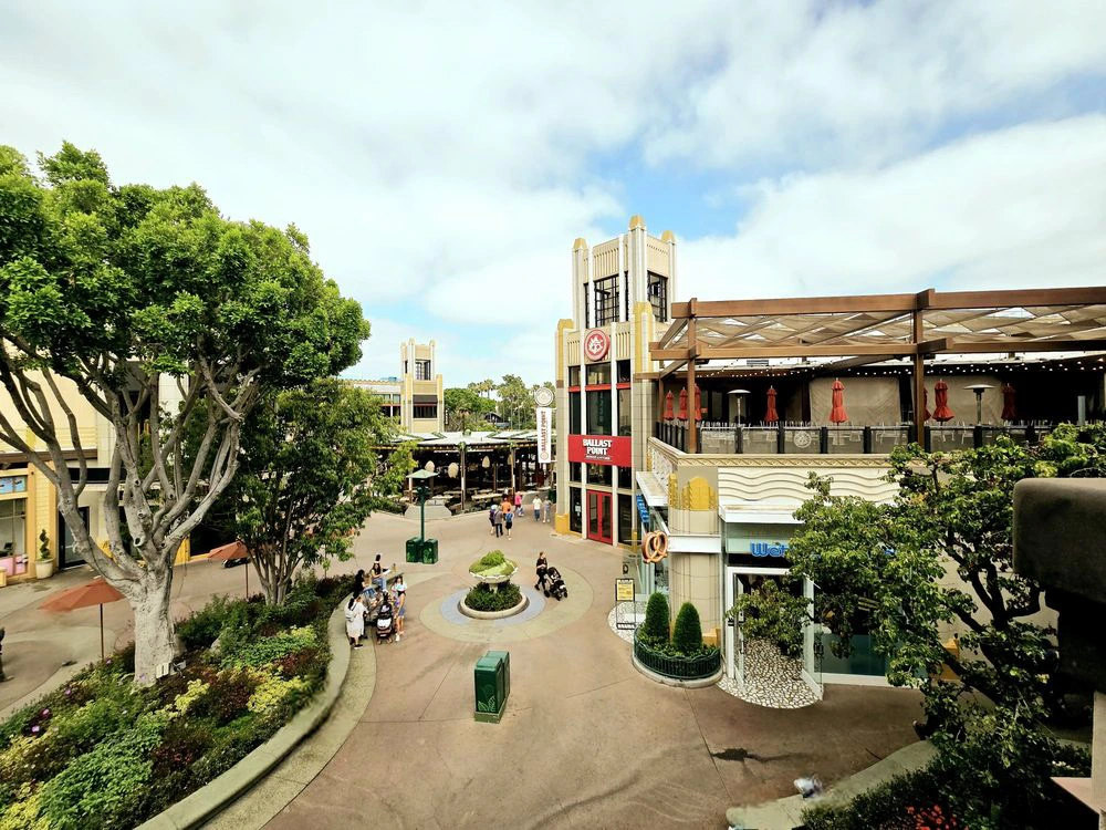 Elevated daytime view of the lush walkways and storefronts along the vibrant Downtown Disney promenade.