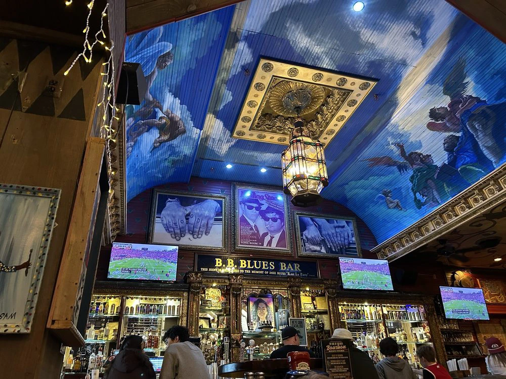 Patrons sit at an ornate wooden bar under a vibrant blue painted sky ceiling inside House of Blues at Disney Springs.