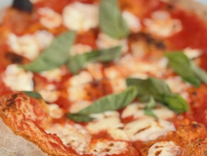 Close-up of a freshly baked wood-fired Margherita pizza with melted mozzarella and fresh basil leaves.