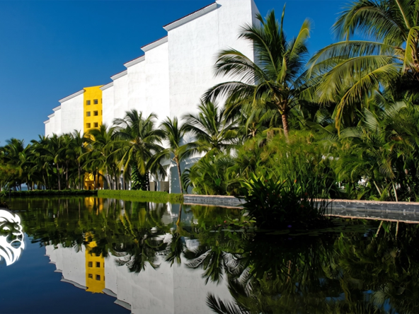 White stepped architecture of Mayan Palace reflected in a tranquil water feature surrounded by palms.