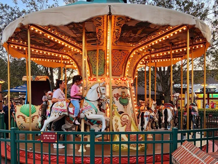 Children and parents ride ornate painted horses and carriages on a glowing, colorful vintage carousel at twilight.