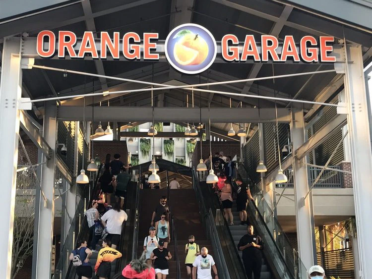 Visitors ride escalators and ascend stairs under the large covered exterior parking structure at Disney Springs.
