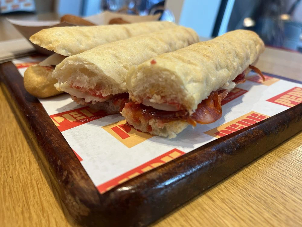 Three slender, toasted Spanish-style baguette sandwiches layered with cured meats and cheese on a wooden serving board.