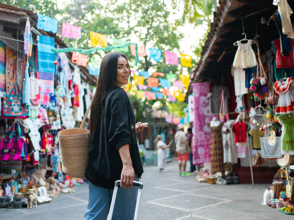 Smiling traveler rolling a suitcase through a lively Puerto Vallarta market hung with colorful paper flags.