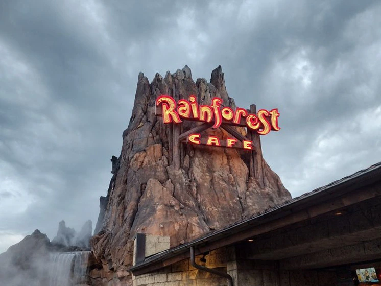 A glowing neon sign sits on a large artificial volcano with steam rising from a rocky waterfall at Disney Springs.