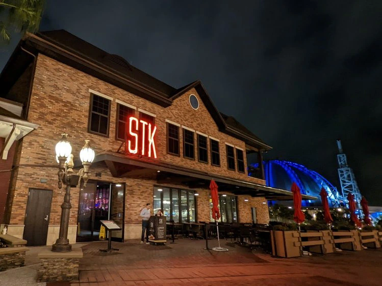 A classic two-story brick steakhouse at night illuminated by a glowing red neon sign, with a glowing streetlamp in front.
