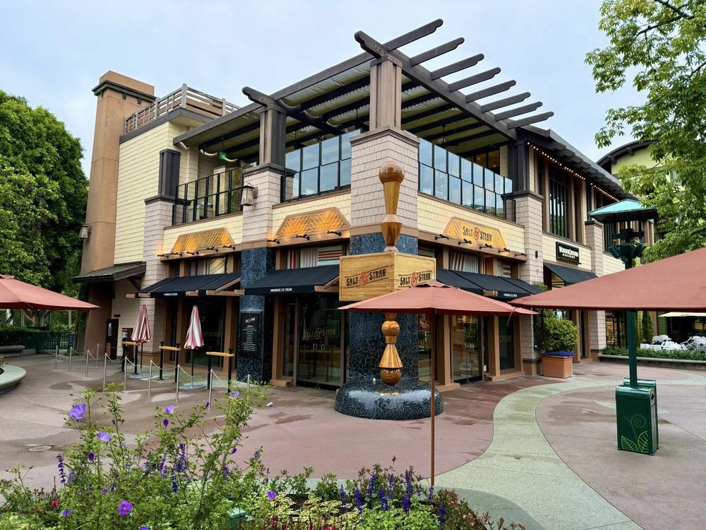 Exterior of the Salt & Straw shop featuring patio umbrellas and a prominent wooden ice cream scoop sculpture.