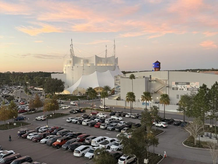 An elevated sunset view over an active outdoor parking lot beside the large white circus tent theater at Disney Springs.