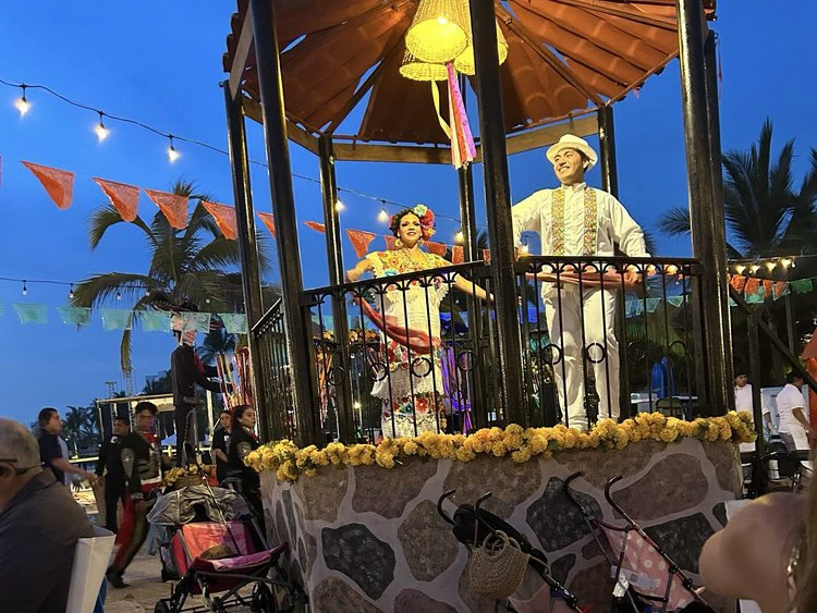 Performers in traditional Mexican dress dancing on a festive gazebo stage.