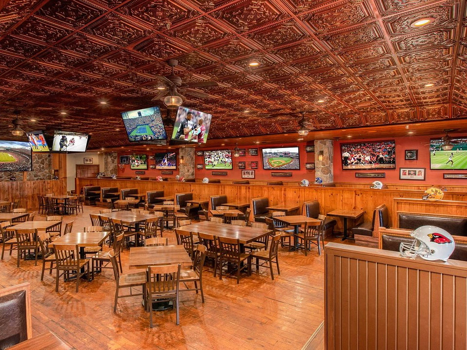 A rustic sports bar interior featuring wooden tables, leather booths, and multiple flat-screen TVs.