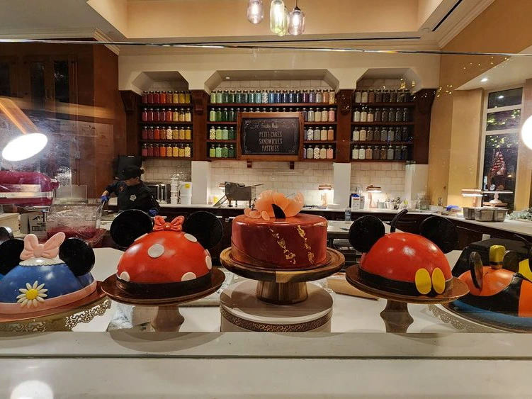 Intricately decorated dome cakes styled like classic cartoon characters displayed in a brightly lit bakery pastry case.
