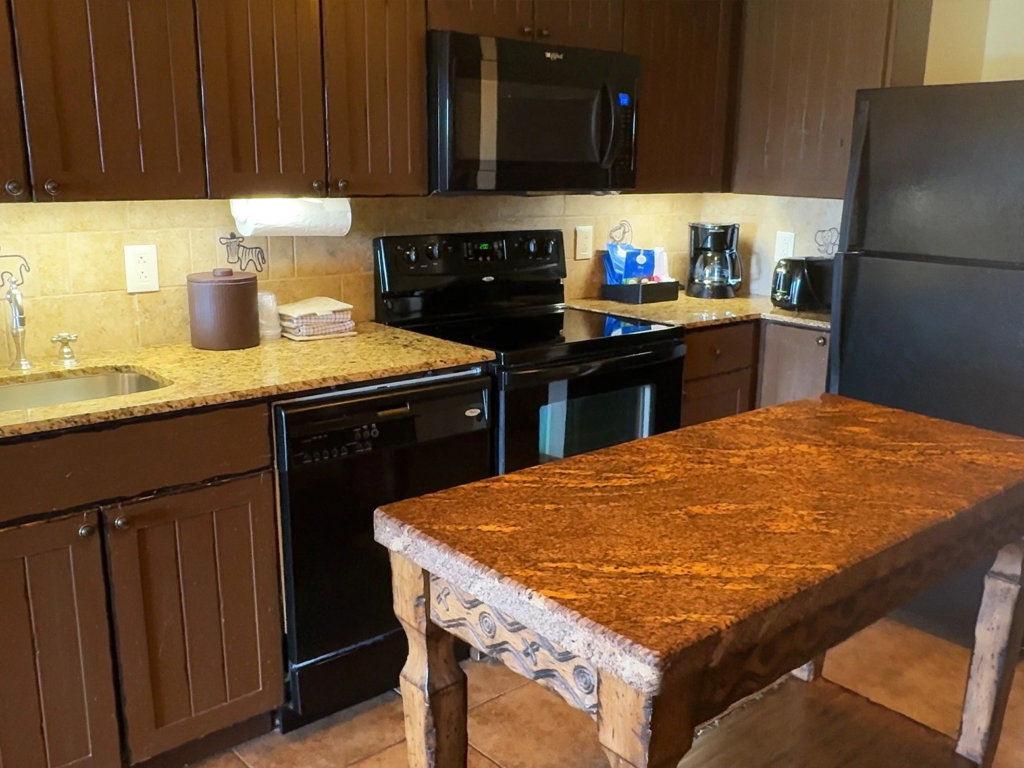 A timeshare villa kitchen featuring dark wood cabinets, black appliances, and a granite island at Jambo House.