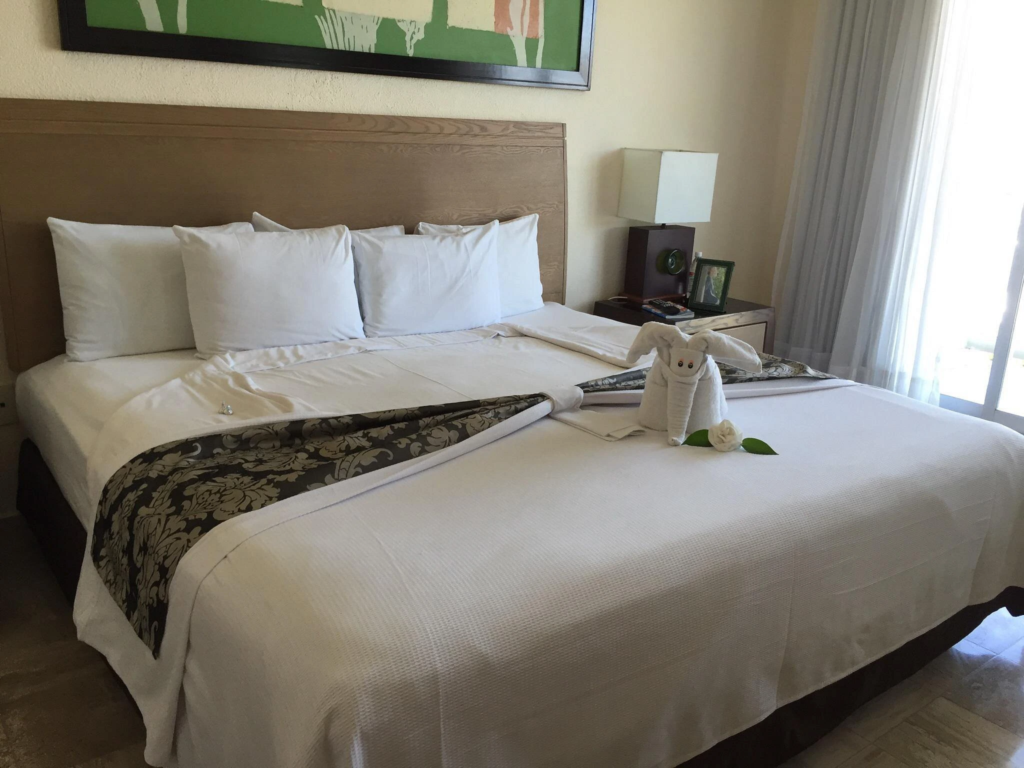 King bed featuring a decorative towel elephant and white linens inside a bright Mayan Palace resort bedroom.